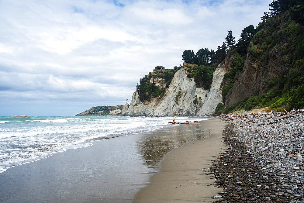 Secluded beach with crashing waves, pebbled shore, and towering white cliffs at Gore Bay Beach, South Island, New Zealand