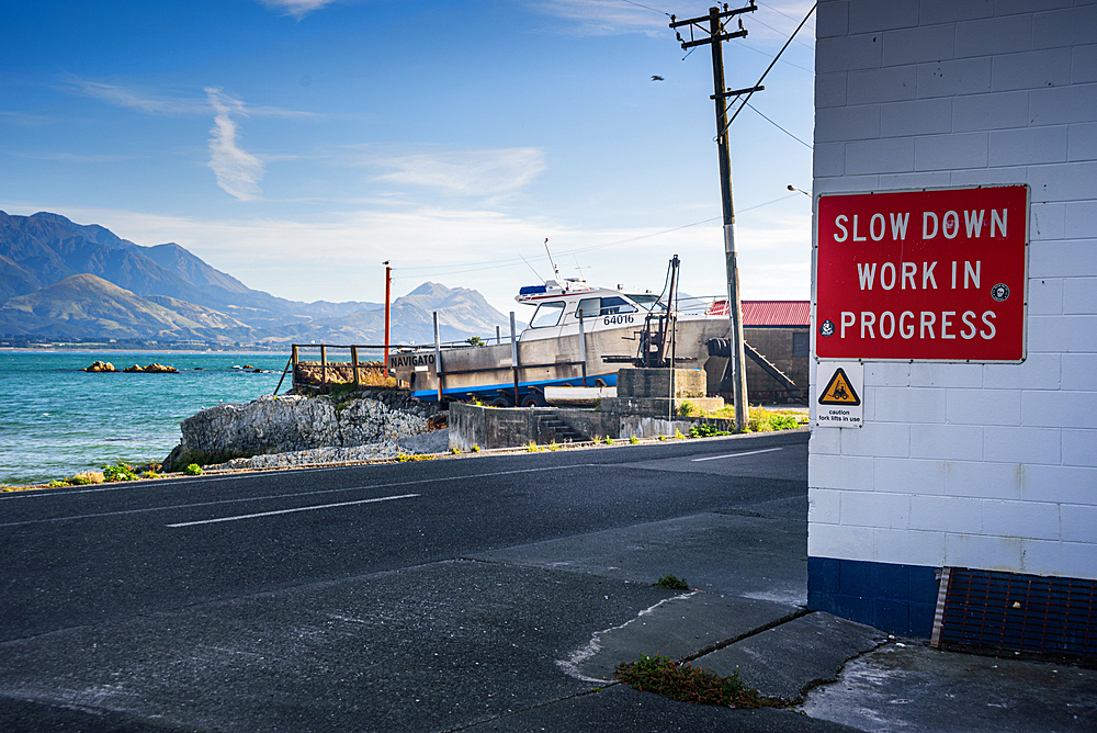 Coastal road beside blue sea with mountain views and work in progress sign at Kaikōura Peninsula, South Island, New Zealand