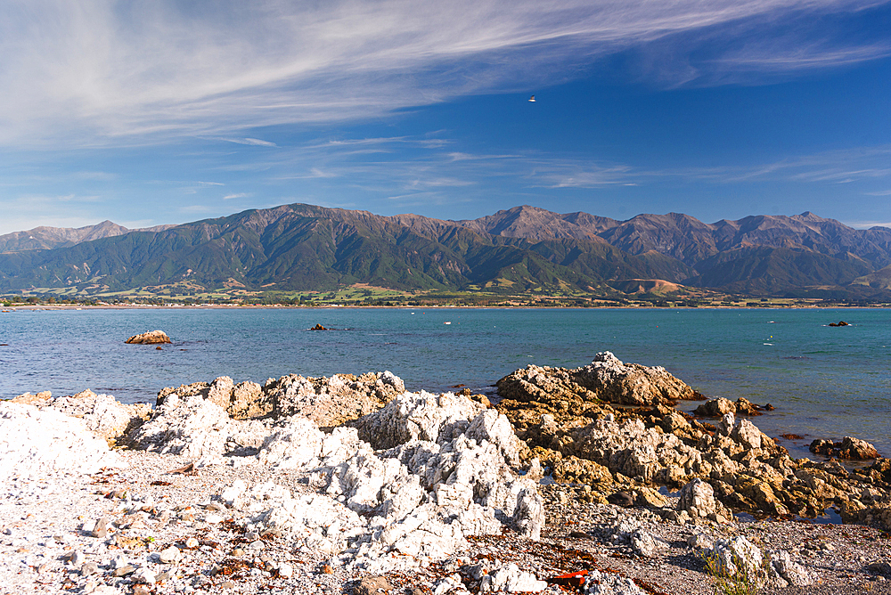 Rocky shoreline with dramatic mountain backdrop under blue sky at Kaikōura Peninsula, South Island, New Zealand
