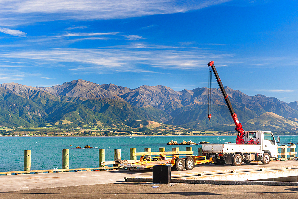 Red Crane Truck on Sunny Wharf with Coastal Mountains and Calm Sea in South Bay Harbour, Kaikoura Peninsula, New Zealand