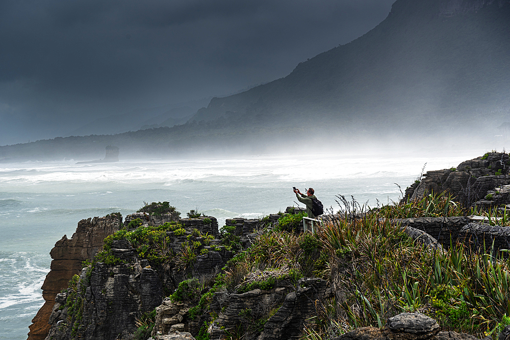 Tourist Taking a Selfie on Windy Cliff Edge Above Crashing Surf at Pancake Rocks, Punakaiki, Paparoa National Park, West Coast, New Zealand