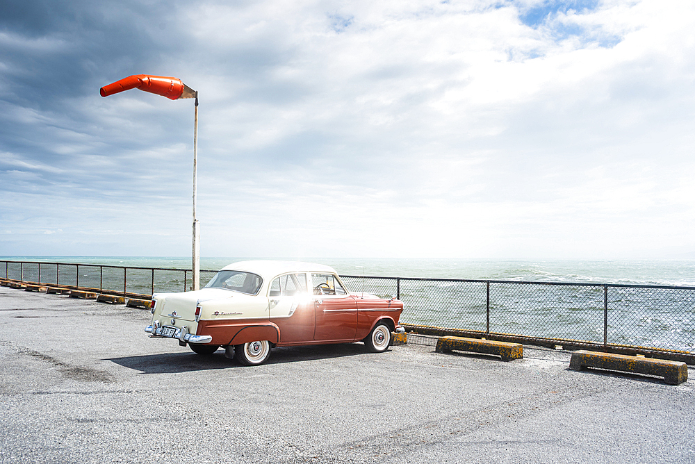 Classic Red Car Parked by the Sea with Windsock Blowing on Windy Day at West Coast Lookout, New Zealand