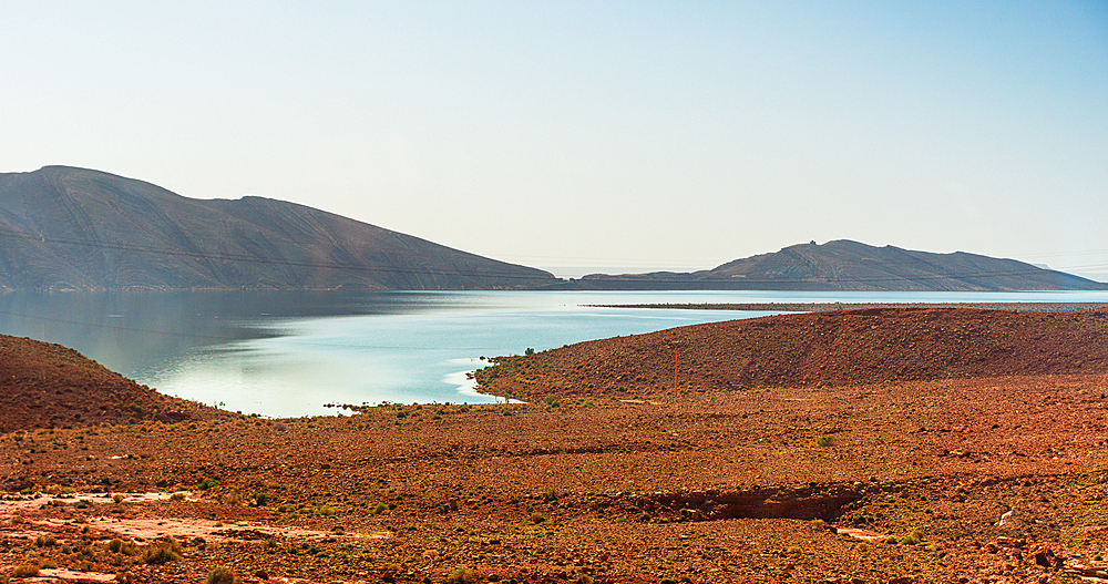 Narrow winding inlet of Barrage Al-Hassan Addakhil glistening between rolling red hills in Parc National Al Hassan Addakhil