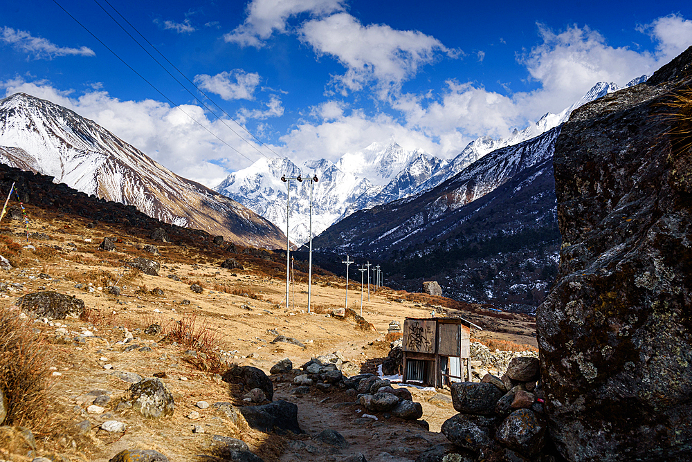 Small shelter and prayer flags along mountain path with stunning view of snow-covered Gangchempo, Langtang Himalay, Nepal