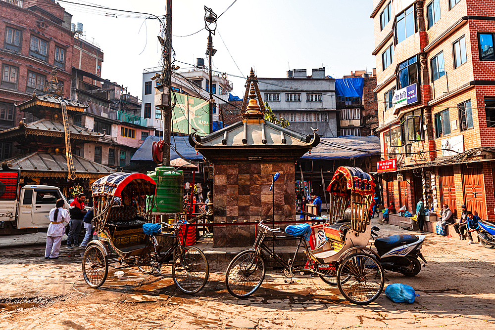 Small stupa surrounded by rickshaws and people in a Kathmandu street, blending religion and urban life