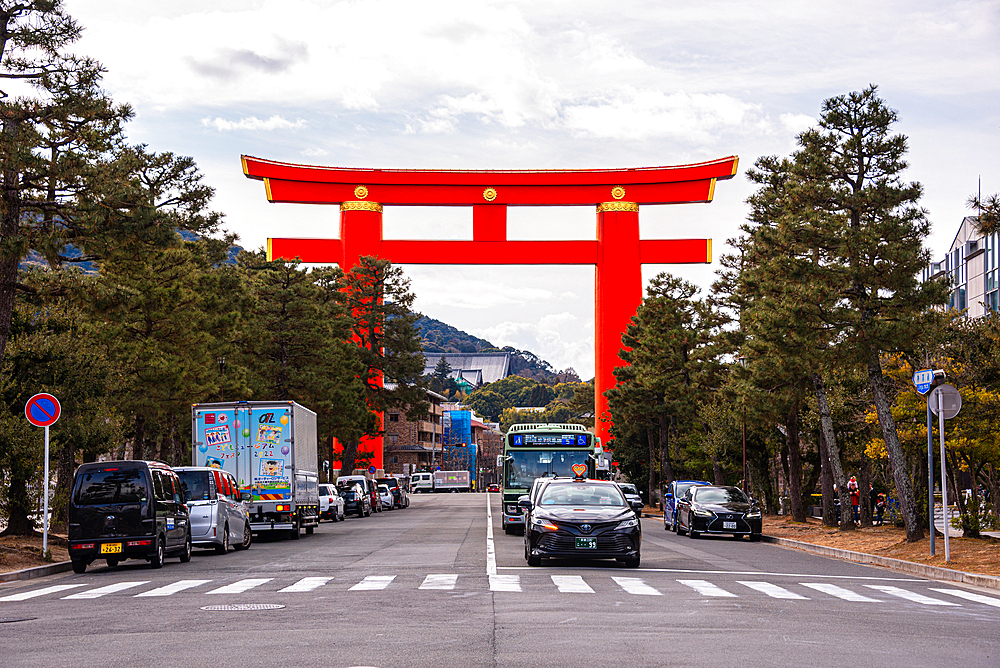 Red torii gate over a busy street filled with cars and lined with trees, leading toward Heian Shrine in Kyoto, Japan