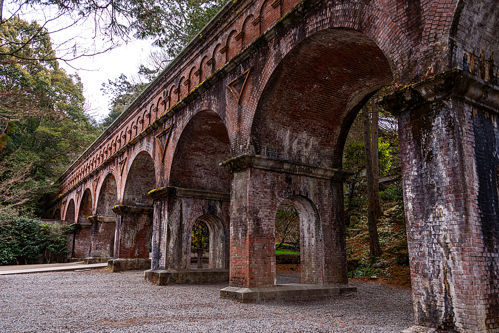 Historic red brick arches of the Suirokaku Aqueduct nestled among tall cedar trees in the temple grounds of Nanzen-ji, Kyoto