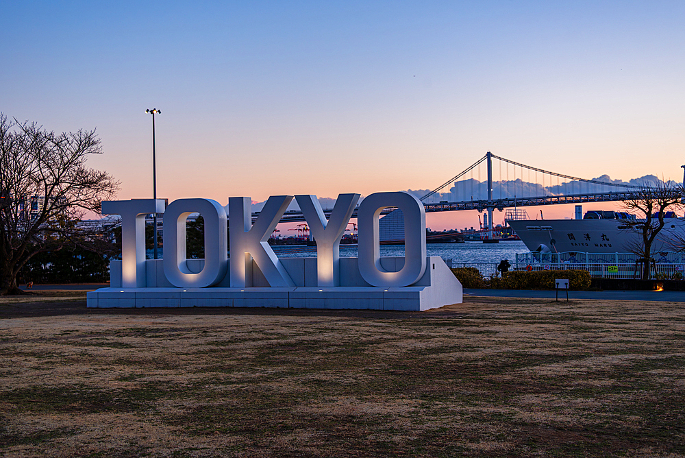 Sunset view of Tokyo’s iconic waterfront with large TOKYO sign in Odaiba and Rainbow Bridge spanning Tokyo Bay in the background