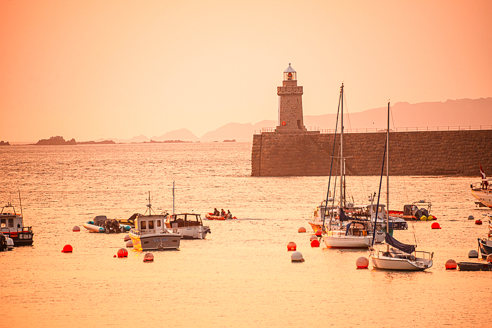 Fishing boats and lighthouse at a hazy sunrise on the harbour of St Peter Port, Guernsey, Channel Islands. Castle Breakwater Lighthouse