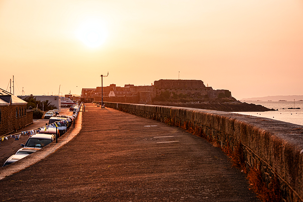 Golden sunset over the stone harbour walkway with Castle Cornet Rock in St Peter Port, Guernsey, Channel Islands.