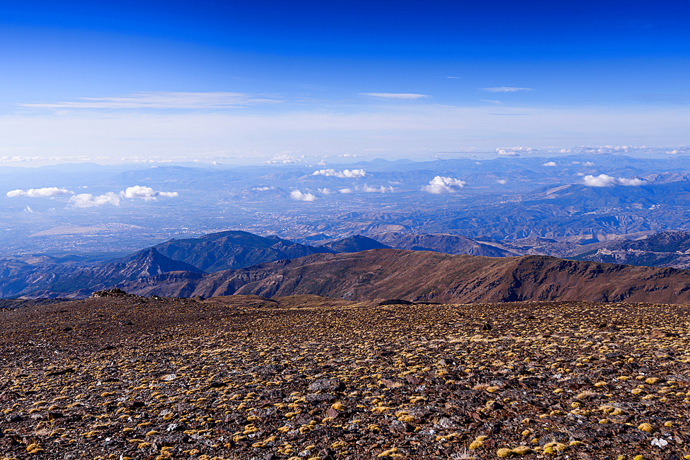 Panoramic view from the upper slopes of Sierra Nevada National Park, Andalusia, Spain. The vast plateau stretches towards Granada province under clear blue skies.