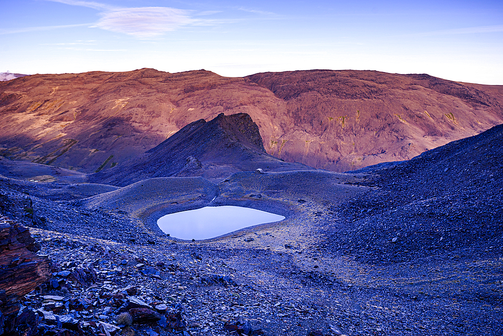 Alpine glacial lake near Pico del Caballo, glowing at sunset in Sierra Nevada National Park, Andalusia, Spain. The remote mountain lagoon reflects the rugged peaks of the highest mountain range in southern Spain.
