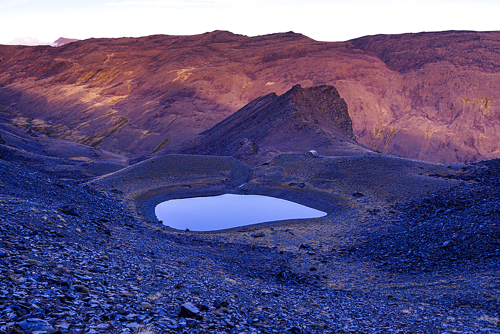 Glacial lake Piedra de los Capuzones glows at dusk among rugged peaks in the Sierra Nevada, Andalusia, Spain.