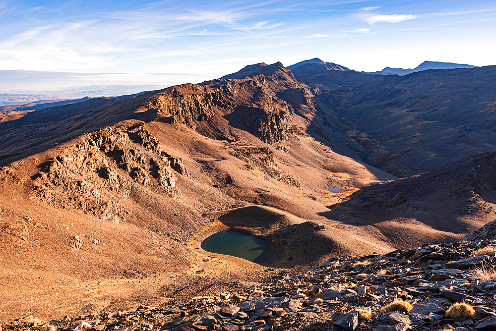 A high-altitude lake lies beneath rocky ridges near Pico del Caballo in the Sierra Nevada, Andalusia, Spain.