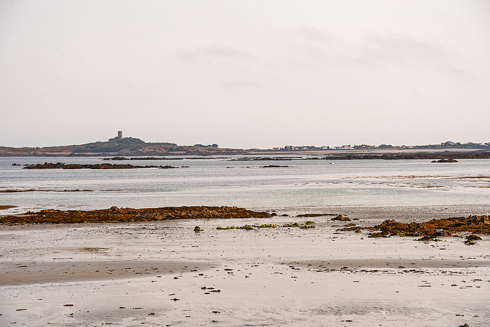 Expansive tidal flats exposed at low tide in Rocquaine Bay, with distant views of Guernsey’s coastline, Channel Islands, United Kingdom.