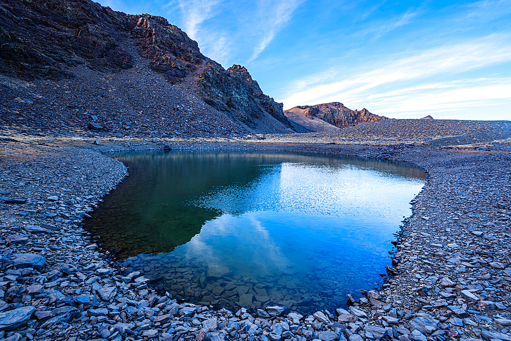 Clear mountain reflections in a high alpine tarn near Cerro del Caballo in Sierra Nevada National Park, Andalusia, Spain.