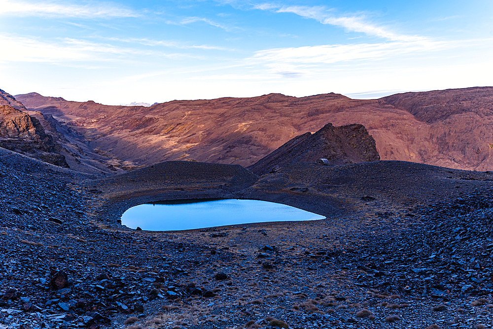 A pristine glacial tarn reflecting morning light beneath Cerro del Caballo in Sierra Nevada National Park, Andalusia, Spain.
