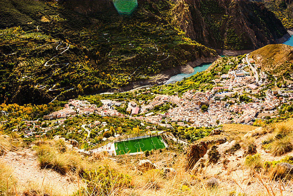 Aerial view of the white washed village of guejar sierra on the foot of the Sierra Nevada next to the blue guerja Embalse lake.