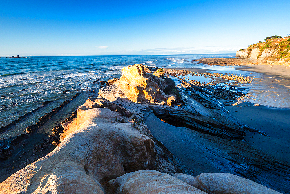 Rocky shoreline with dramatic cliffs and Tasman Sea waves at low tide, Cape Foulwind, South Island, New Zealand.