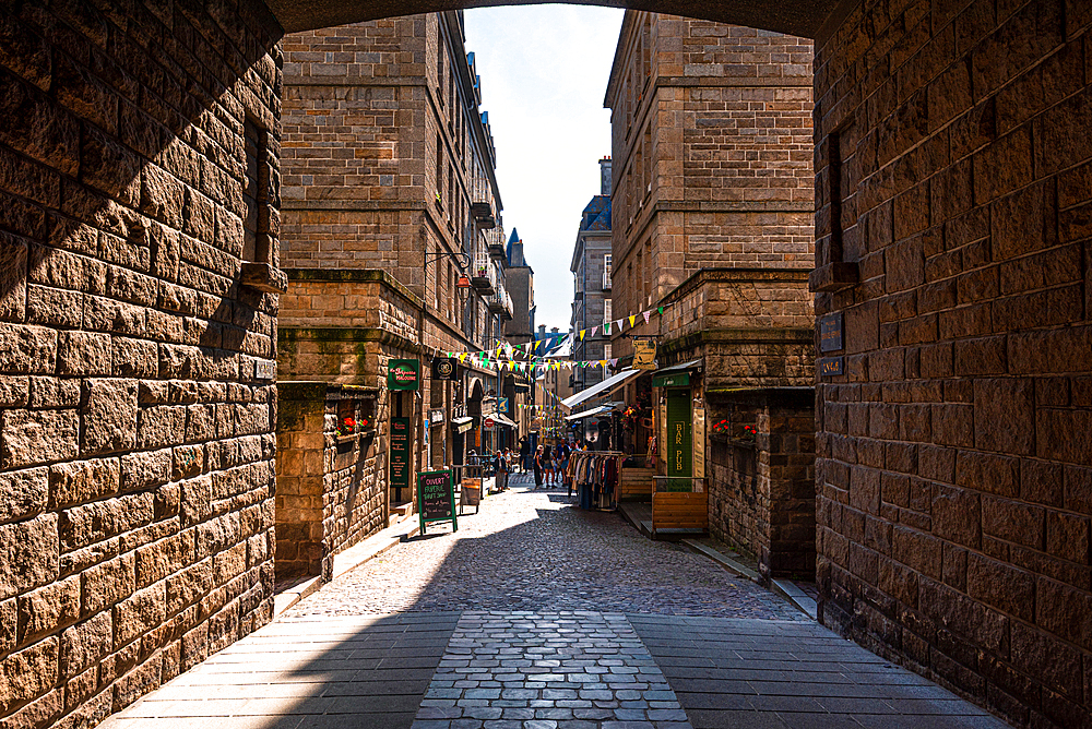 Quiet cobbled alleyway with stone houses inside the fortified walls of Saint-Malo, Brittany, France, illuminated by afternoon light
