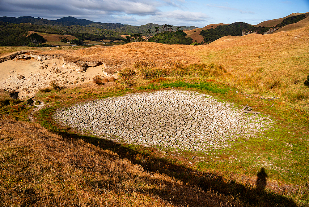 Arid farmland in New Zealand’s South Island with dried pond and golden grass hills under summer drought conditions.