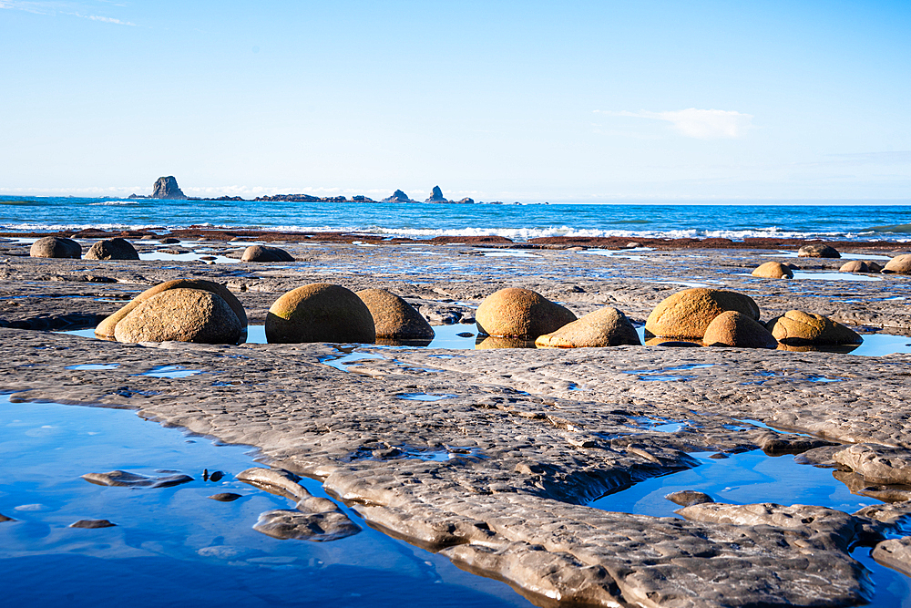 Rounded boulders on Cape Foulwind beach at low tide with Tasman Sea and West Coast cliffs South Island New Zealand