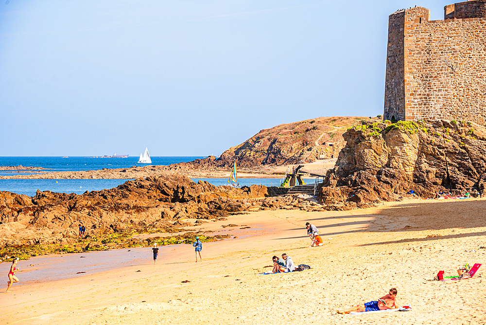Tourists on sandy beach by Saint-Malo city walls and rocky coast Brittany France