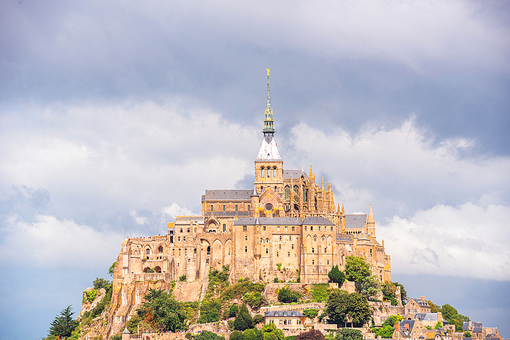 A dramatic view of Mont Saint-Michel Abbey, Normandy, France, rising above the village with its Gothic spire pointing to the sky.
