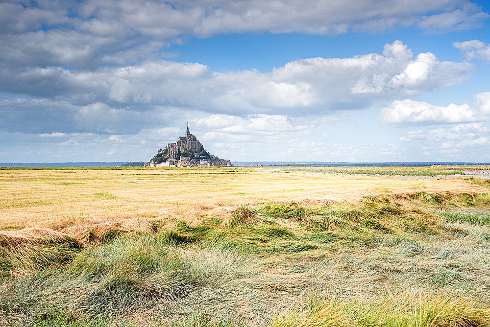 A sweeping landscape view of Mont Saint-Michel, Normandy, France, rising dramatically from the vast tidal flats that surround the island.