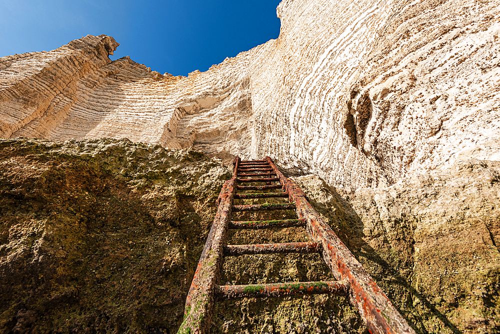 Rustic metal ladder steps descend toward the towering limestone walls of Étretat’s cliffs on the Normandy coast.