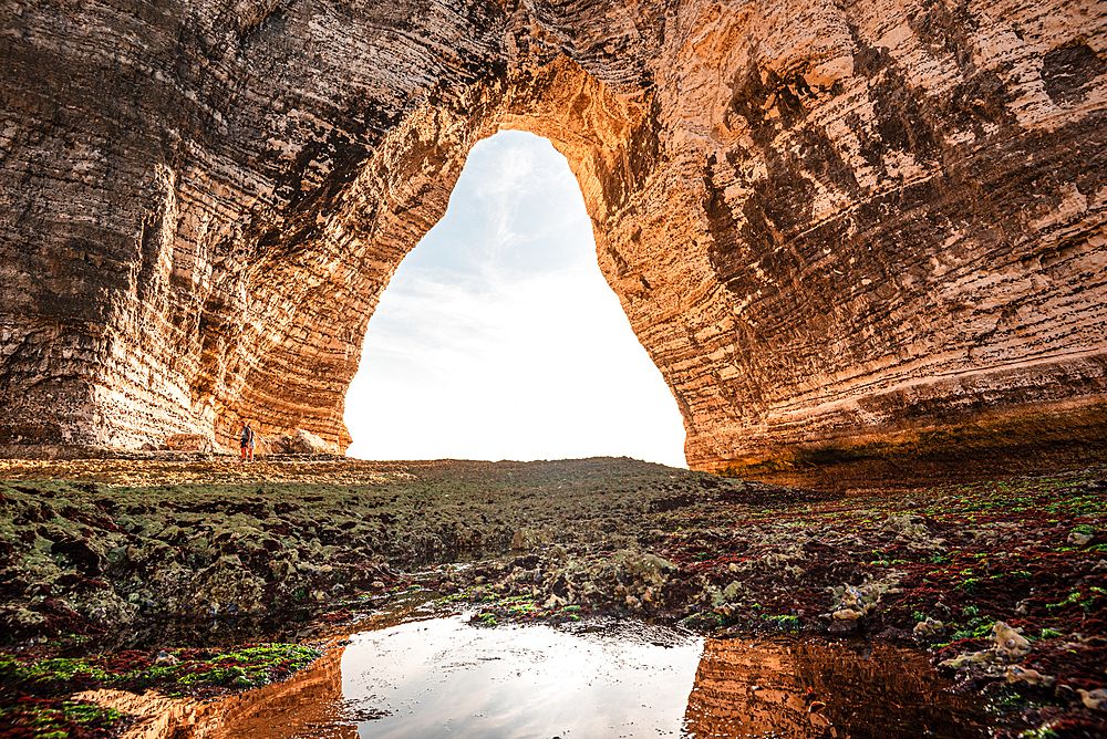 Perspective from inside a sea cave at Étretat, Normandy, looking out toward the sky through a natural chalk arch.