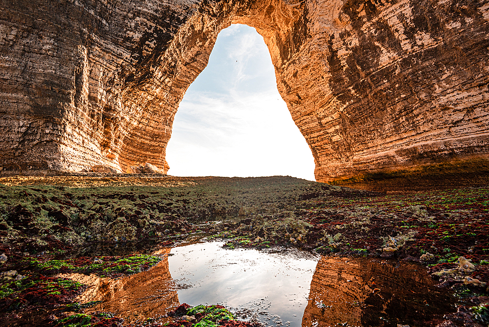 Dramatic coastal scene from the Étretat cliffs in Normandy, with a chalk arch opening toward the English Channel.