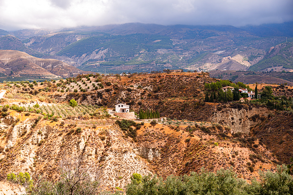 Andalusian countryside near Durcal with isolated farmhouses, olive groves, and rugged badlands leading to distant mountains.