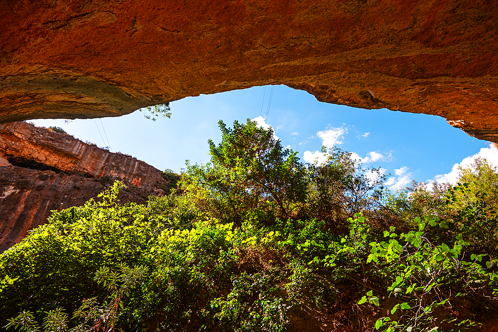A natural rock arch frames green vegetation along the Barranco de Luna trail, highlighting the contrast between rugged sandstone and lush foliage.