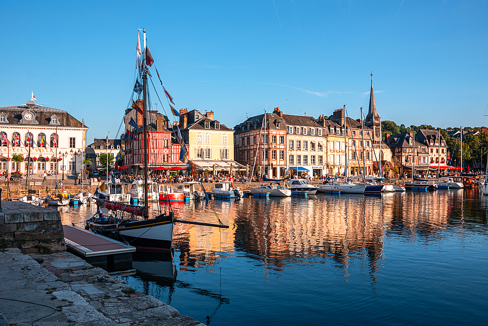 Evening light over the picturesque Vieux Bassin in Honfleur, highlighting old stone buildings, sailing boats, and the famous wooden church spire.