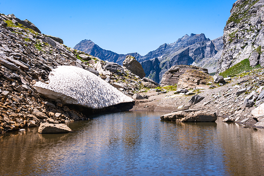 Remains of a snow field in the Alps melting into a lake on an alpine mountain pass, the Alps, Piemonte (Piedmont) Northern Italy, Europe