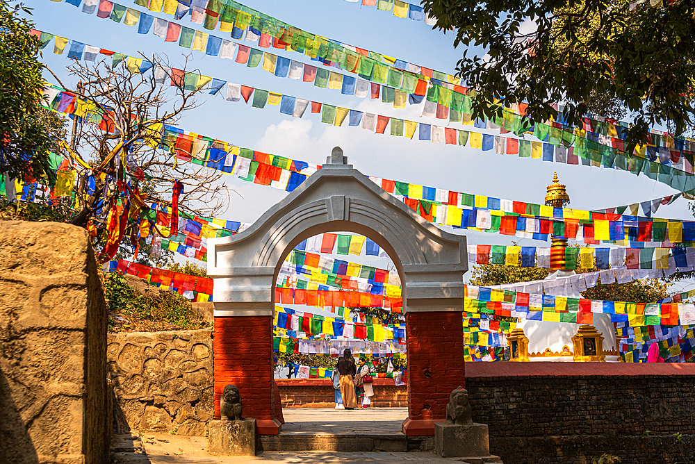 Stone arch gate leading to Kashyap Stupa with colorful Buddhist prayer flags, Kathmandu, Nepal, Asia