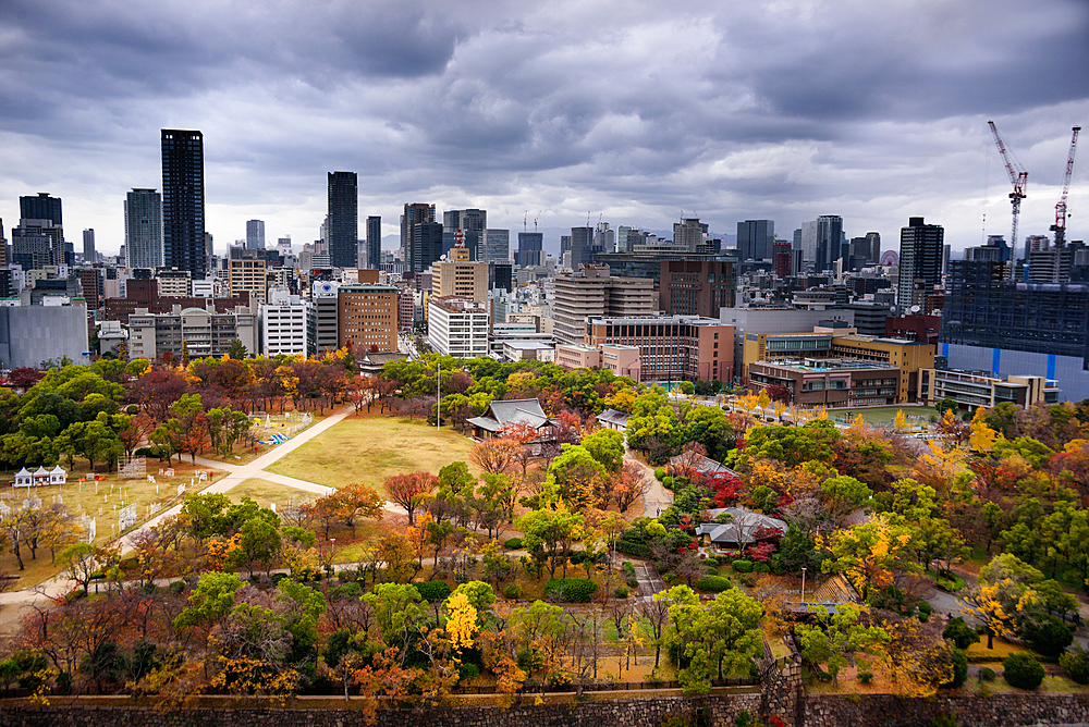 Looking over the castle park onto the city skyline with dramatic sky in autumn, Osaka, Honshu, Japan, Asia