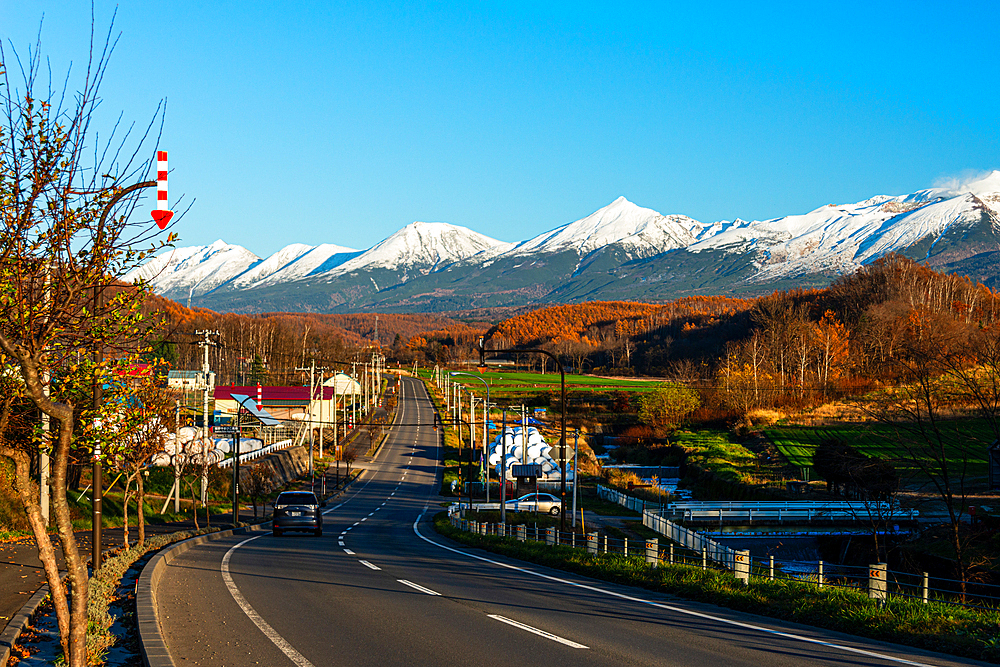 Alpine panorama of rural area with highway leading to the snowy Tokachi mountain range in Hokkaid , Japan, Asia