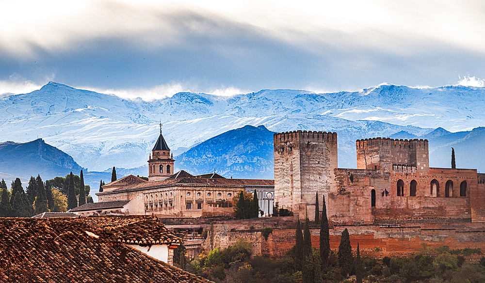 Winter coming to Granada, Spain. Snowy Sierra Nevada with pico de Veleta beind the warm colored Alhambra. iconic Moorish fortress showcases historic architecture with warm tones, contrasting against the crisp mountain landscape