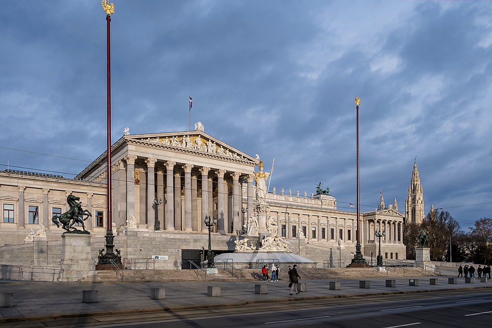 Vienna, Austria – View of the Austrian Parliament's grand neo-Greek entrance facade on Ringstrasse, featuring the monumental Pallas Athena fountain and sculpted ramp of the Theophil Hansen-designed building.