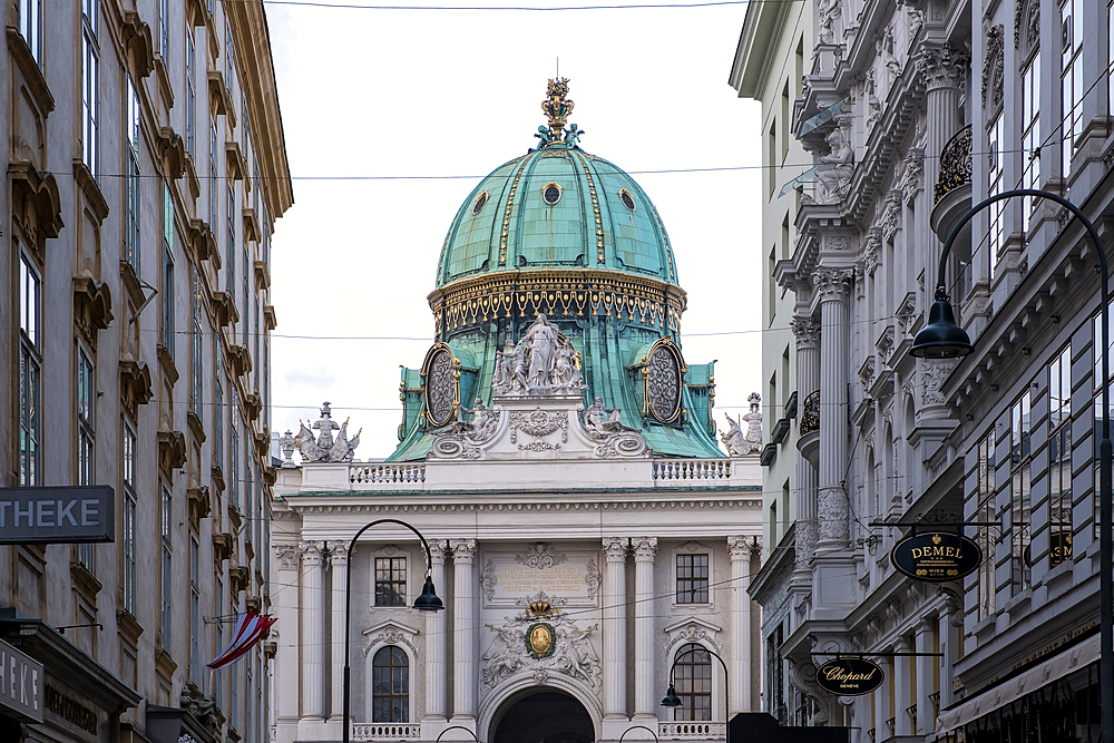 Vienna, Austria – View of Michaelerplatz from Kohlmarkt street, showcasing the square's elegant Baroque architecture with the dome of St. Michael's Wing and the symmetrical facades of surrounding palaces.