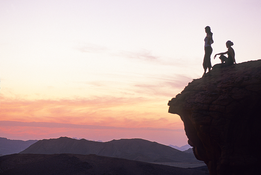 Two women sitting on a rock enjoying sunset in the desert of Wadi Rum, Jordan, Middle East