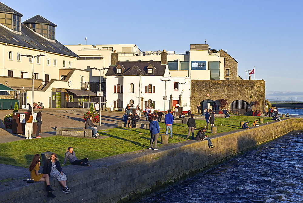 Young people sitting on the banks at the mouth of the Corrib River, downtown Galway, Connemara, County Galway, Connacht, Republic of Ireland