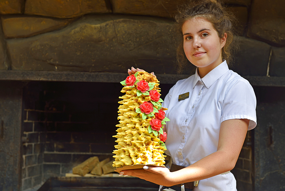 Young waitress presenting a famous cake named Sakotis in a decorated version at Romnesa bakery-restaurant at Strigailiskis, Ignalina district, Aukstaitija National Park, Lithuania, Europe