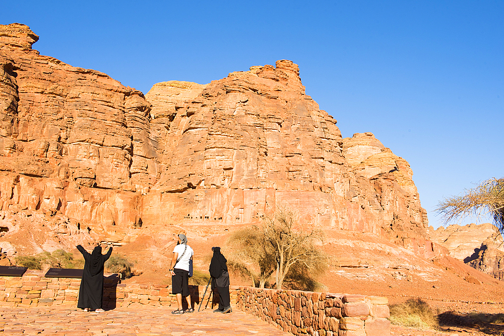 People observing, with binoculars, the tombs cut into the red rock cliffs at Archaeological site of Dadan, the ancient capital of the Dadan And Lihyan kingdoms more than 2000 years ago. AlUla, Medina Province, Saudi Arabia, Middle East