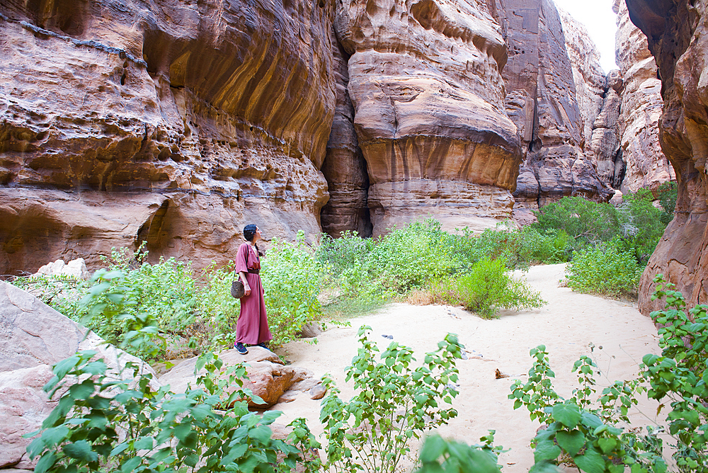 Woman walking at the bottom of a canyon with sandstone walls in the Sharaan Nature Reserve, AlUla, Medina Province, Saudi Arabia, Middle East