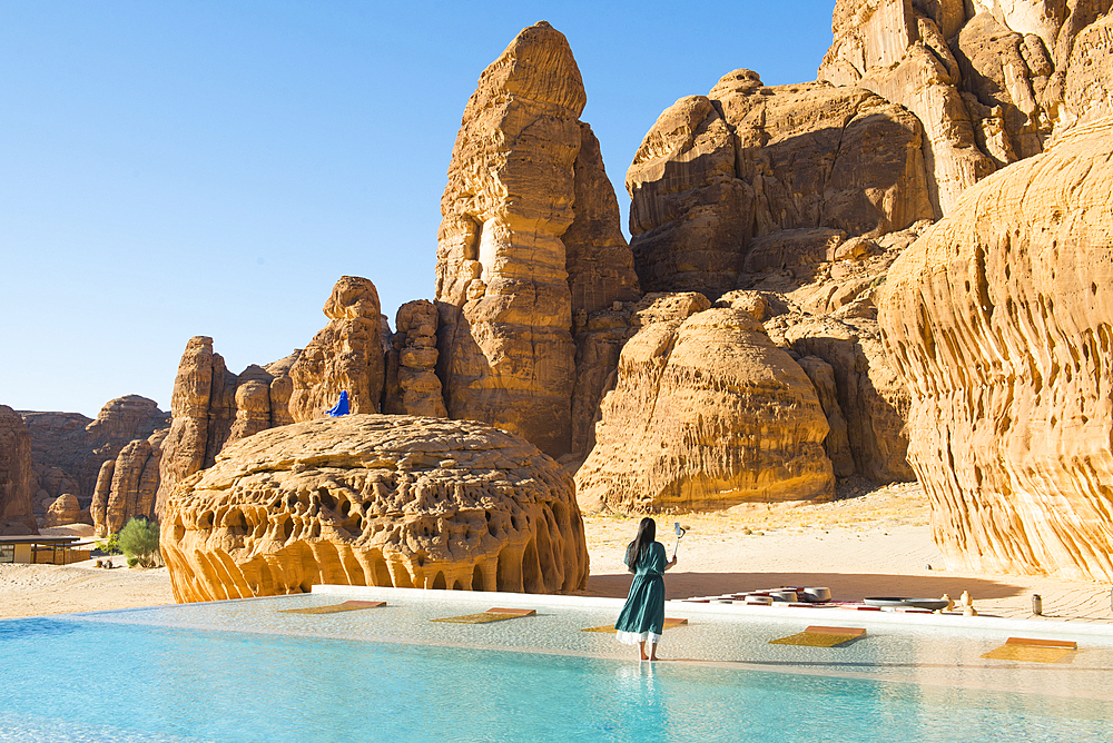 Woman by the Swimming pool, surrended by magnificent sandstone rock structures, of Our Habitas AlUla, a sustainable desert luxury resort nestled within an ancient oasis in the desert canyons of the Ashar Valley, Medina Province, Saudi Arabia, Middle East