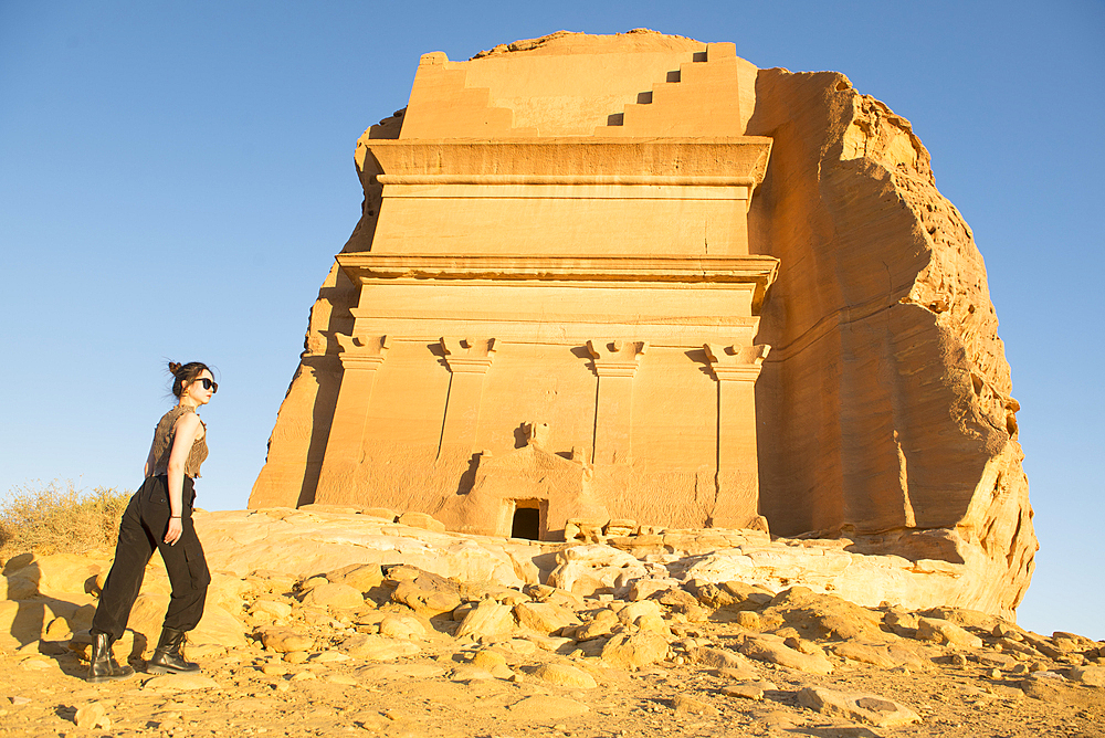 Standing up woman admiring the Tomb of Lihyan son of Kuza (Qasr AlFarid), carved into its own separate sandstone outcrop within the UNESCO World Heritage Site of Hegra, AlUla, Medina Province, Saudi Arabia, Middle East