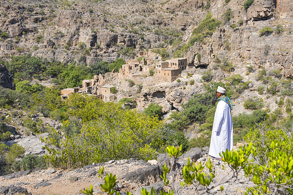 Standing man wearing a dishdasha admiring the old adobe village in ruins of Al Ain, , Perched villages of Jabal Al Akhdar (Green Mountains) around the Sayq plateau, Sultanate of Oman, Arabian Peninsula, Middle East